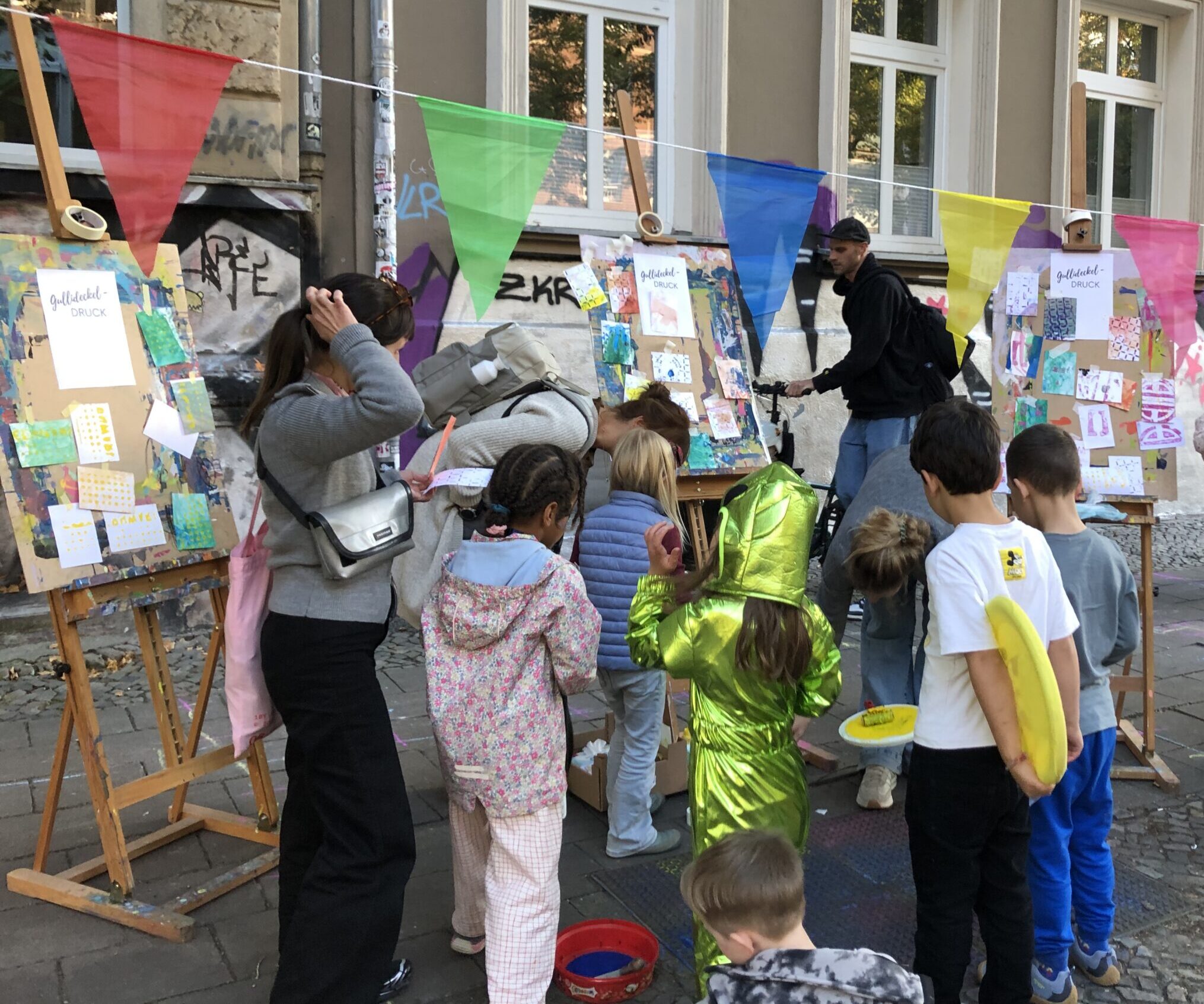 Kinder auf der temporären Spielstraße von oXxymoron in der Scharnweberstraße kreieren bunte Farbdrucke